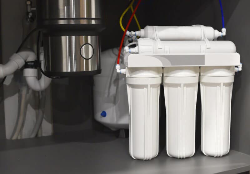 3 white water filter cartridges installed underneath a kitchen sink