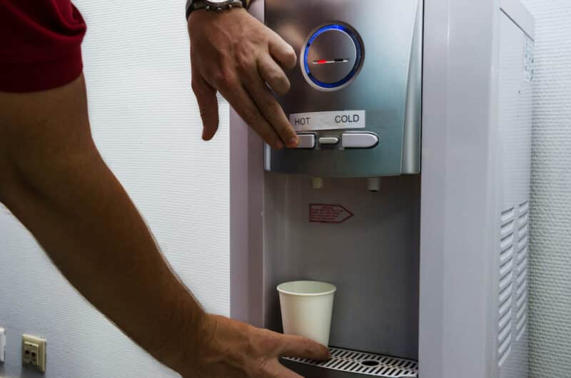 office employee filling a white paper water cup using hot/cold filtered water dispenser