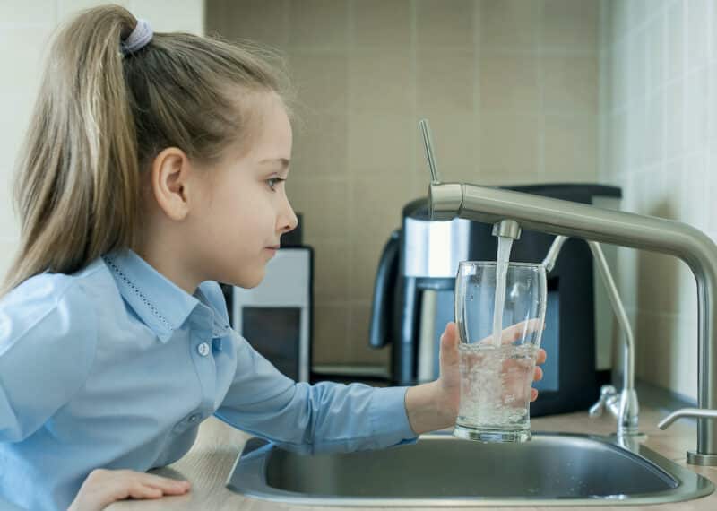 young girl holding glass cup underneath sink faucet, filling it with water