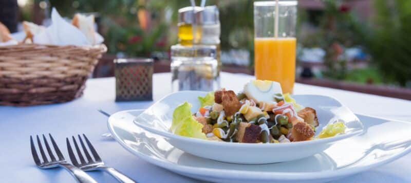 Fresh salad with croutons and a boiled egg on a table with orange juice and condiments