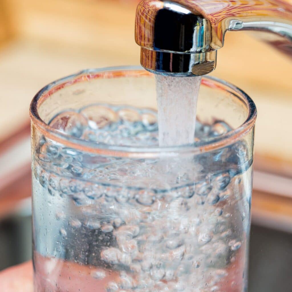 Close-up of a glass being filled with water from a chrome faucet