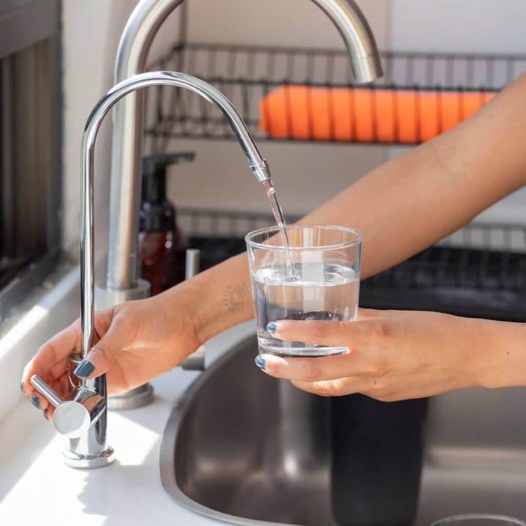 A person filling a glass with water from a modern kitchen filter faucet