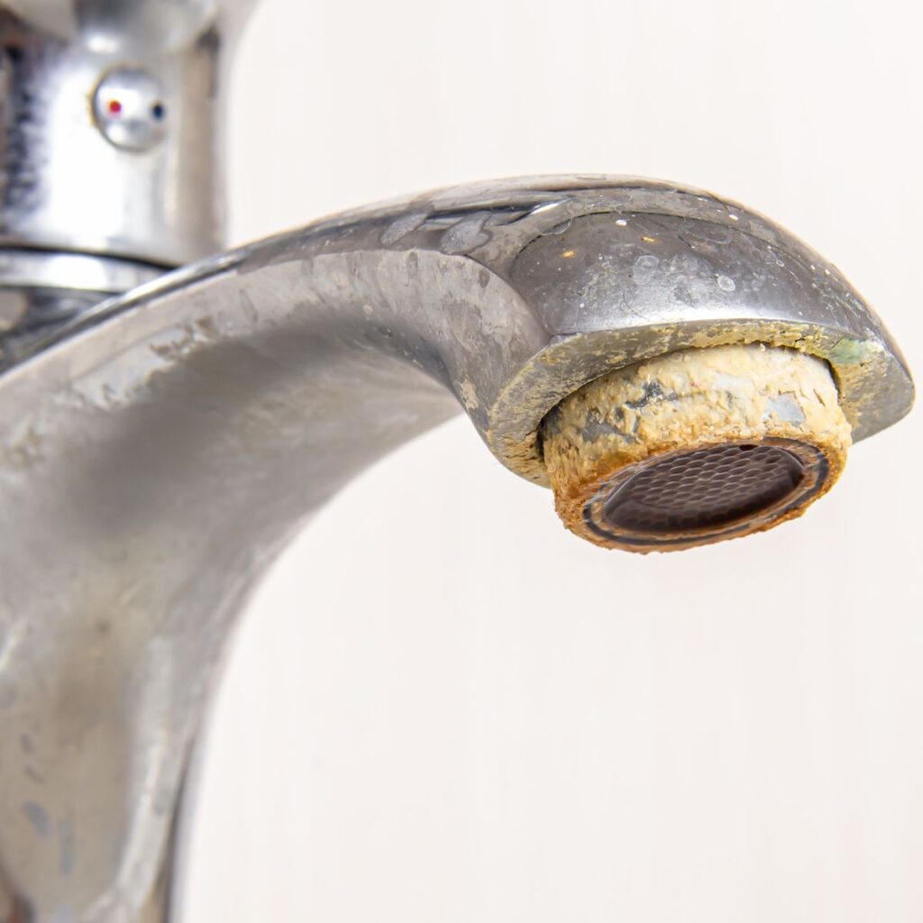 Close-up of a bathroom faucet covered in hard water stains and mineral buildup